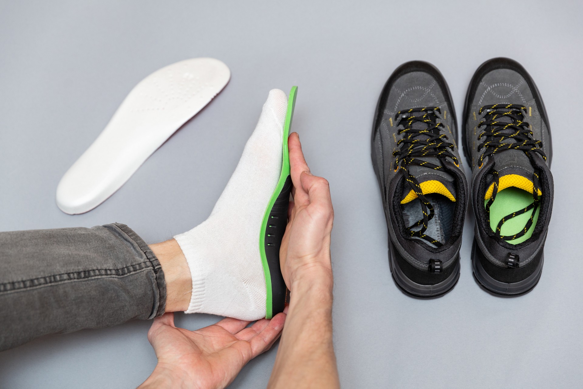 Close up of man hands fitting orthopedic insoles on a gray background.